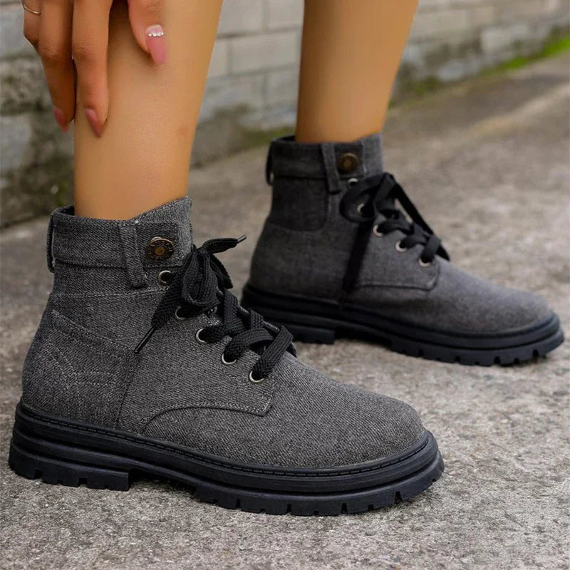 Close-up of gray fabric lace-up ankle boots with black soles on concrete ground