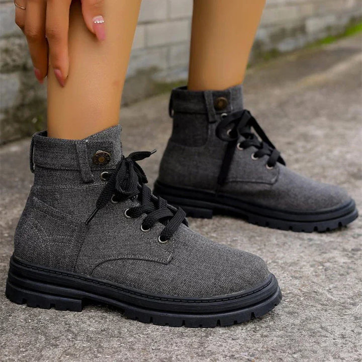 Close-up of gray fabric lace-up ankle boots with black soles on concrete ground