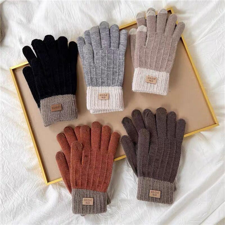 Five pairs of knitted winter gloves in black, gray, beige, rust, and brown with ribbed cuffs and labels, displayed on a beige tray