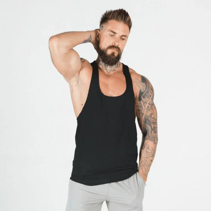 Bearded muscular man with tattoos wearing black tank top and gray shorts on white background