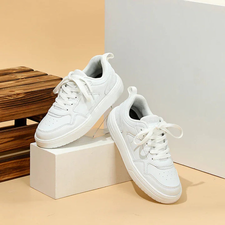 Minimalist white sneakers with lace-up design displayed on beige and wooden background