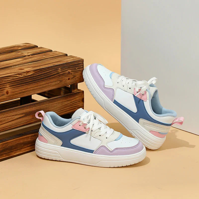 Casual white sneakers with pastel pink, blue, and lavender accents displayed beside wooden crate