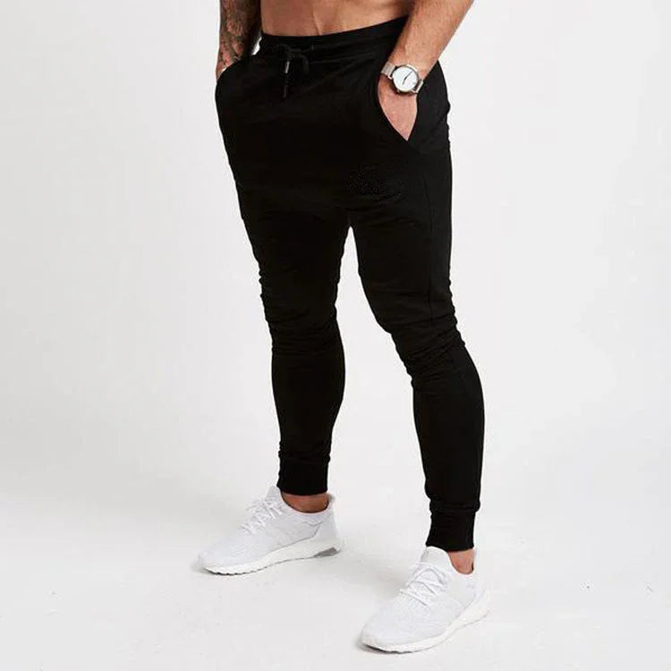 Men's slim fit black jogger pants styled with white athletic sneakers on plain background