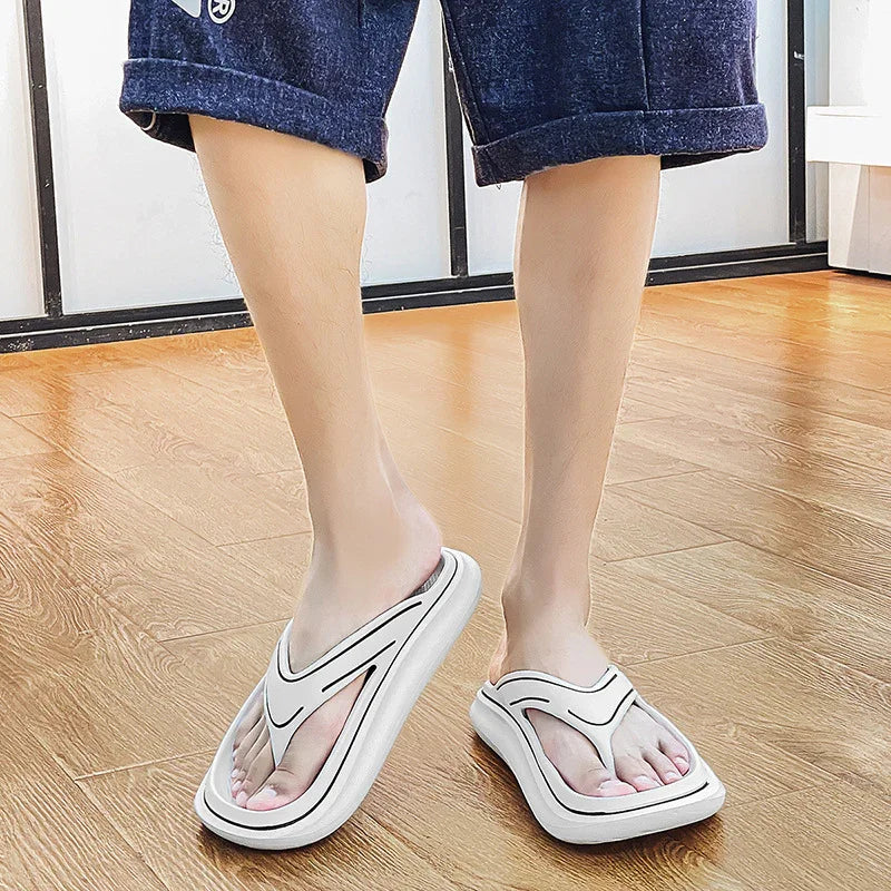 Feet wearing white foam flip flops with black detailing on wooden floor, person in navy shorts