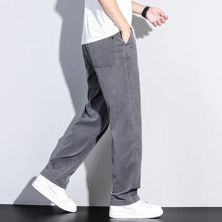 Man wearing loose-fit gray pants with white sneakers and a white t-shirt against plain background