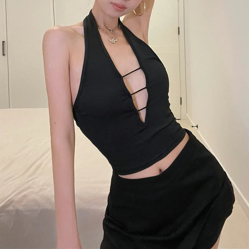Woman wearing a black halter top with deep cut-out and strappy details paired with a black skirt indoors