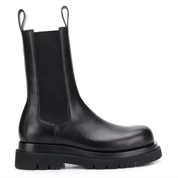 Black leather Chelsea boot with thick rubber sole and pull tabs on white background