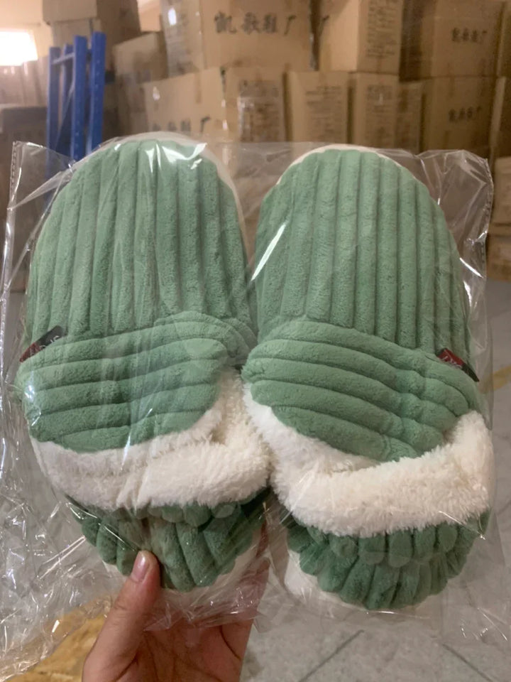 Pair of green corduroy plush winter slippers with white fluffy lining in clear plastic packaging
