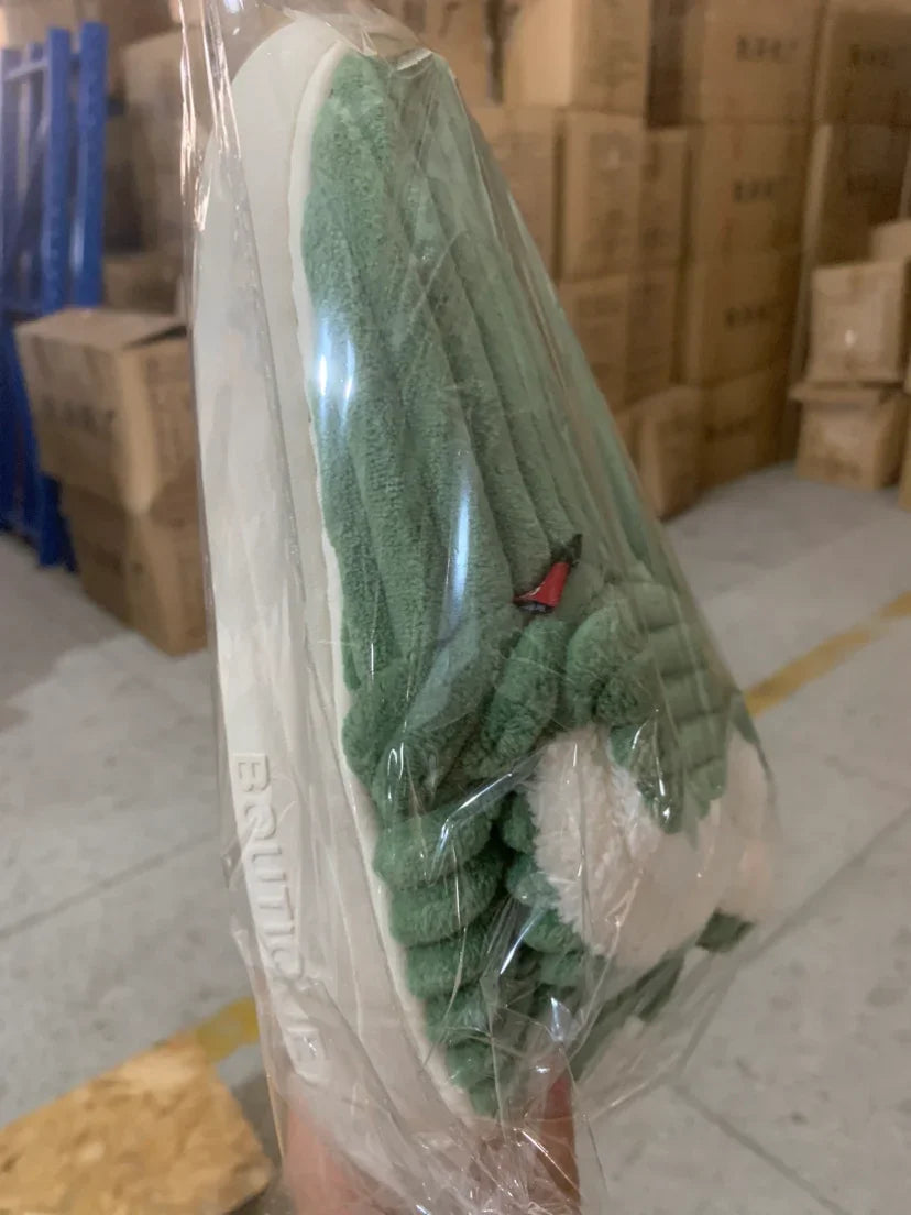 Green and white plush slippers wrapped in plastic, held in hand, warehouse background with stacked boxes