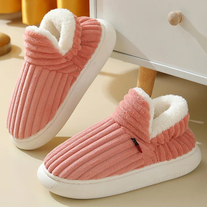 Pink corduroy indoor slippers with white plush lining and thick white soles on beige floor