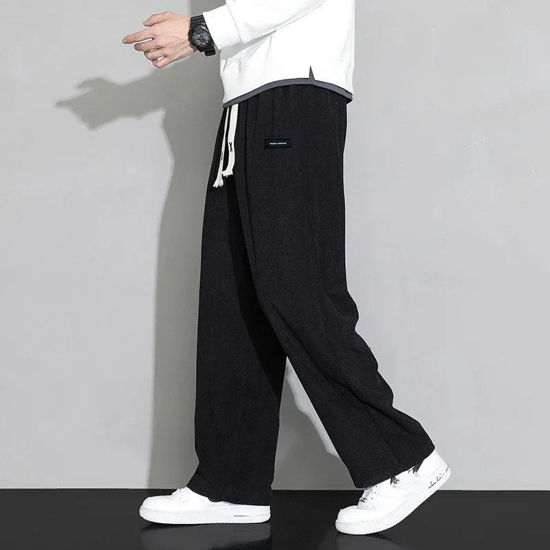 Man wearing black wide-leg pants with white drawstring and white sneakers against gray background
