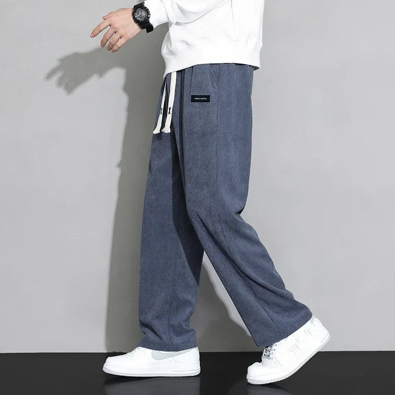 Man wearing loose blue sweatpants with white drawstrings and white sneakers against grey background