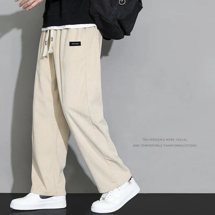 Person wearing beige casual lounge pants with drawstring and white sneakers on grey background