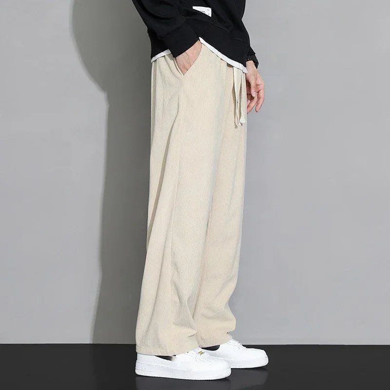 Person wearing loose beige corduroy pants with white drawstrings and white sneakers against grey background