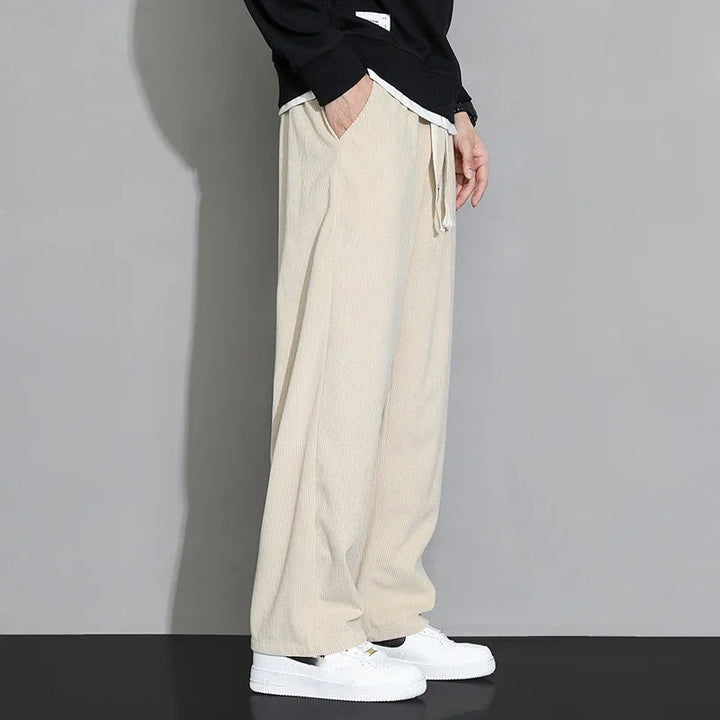 Person wearing loose beige corduroy pants with white drawstrings and white sneakers against grey background