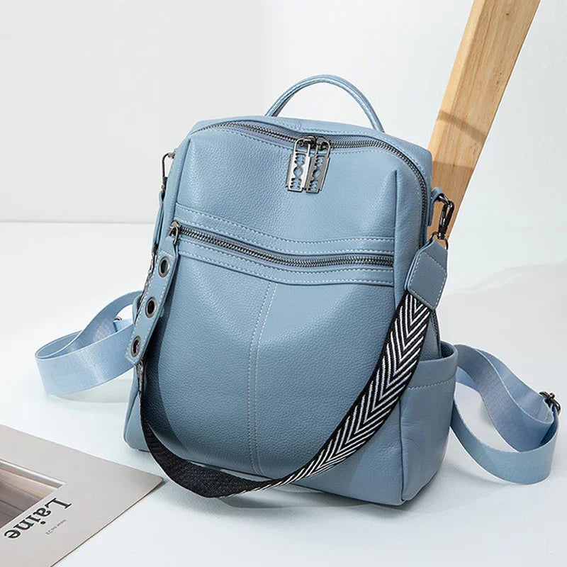 Light blue leather backpack with front zipper pocket and black white chevron strap on white surface