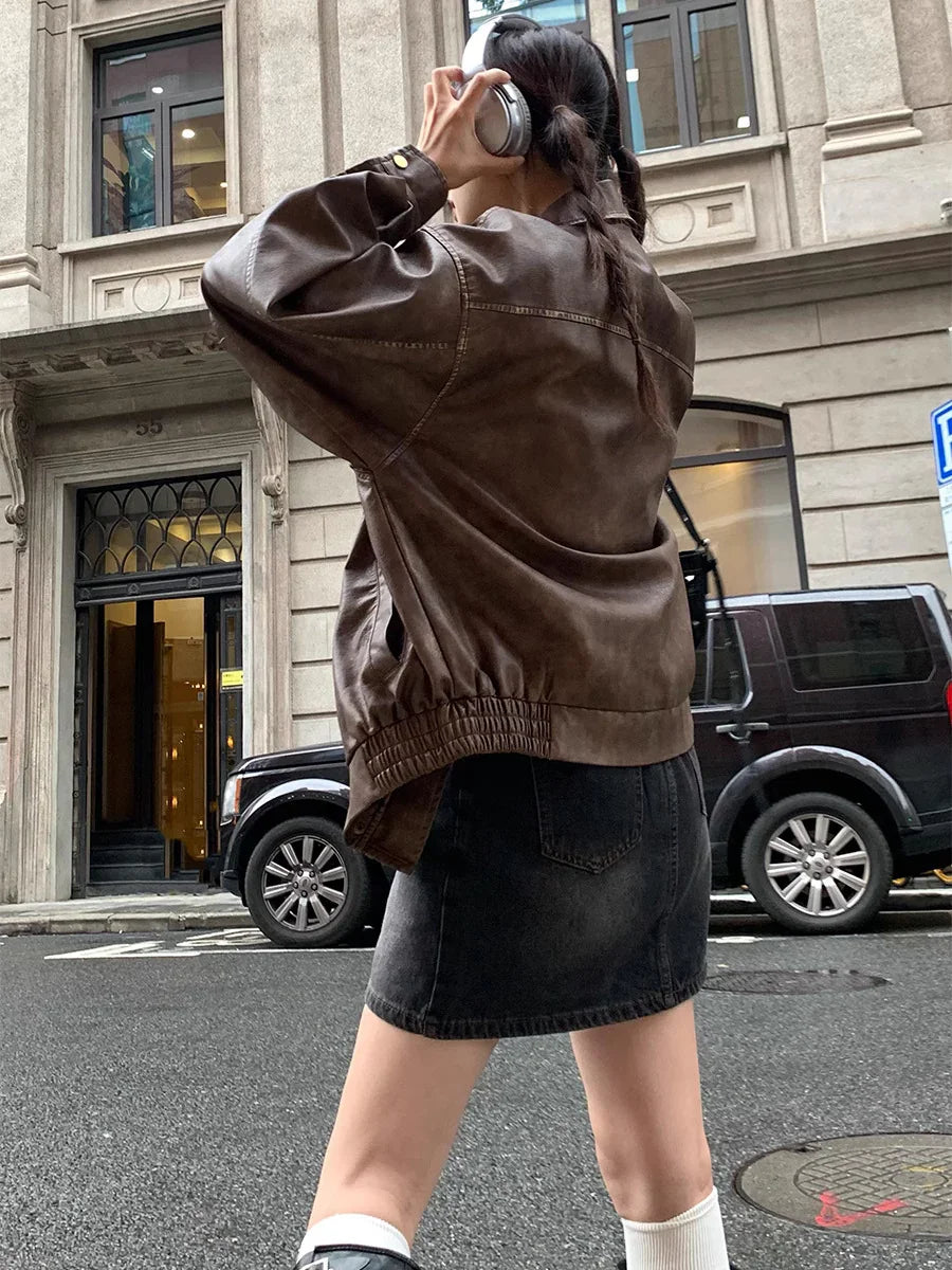 Woman in brown leather jacket and black denim skirt wearing headphones on city street