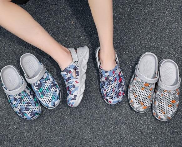 Person wearing colorful patterned slip-on clogs on dark asphalt with two additional pairs nearby