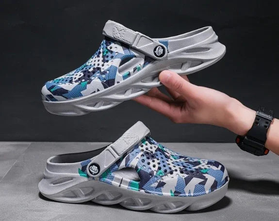 Blue and gray camouflage slip-on clogs with ventilation holes and adjustable straps held against a dark background