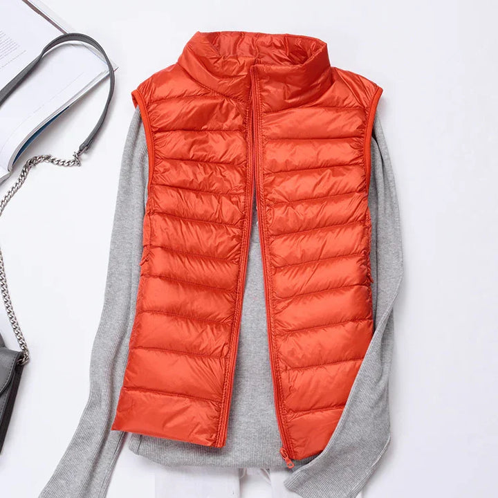 Orange quilted sleeveless puffer vest over light gray long sleeve sweater, styled flat lay