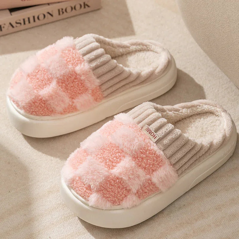 Pair of pink and beige plush checkered indoor slippers with soft padded soles on beige carpet