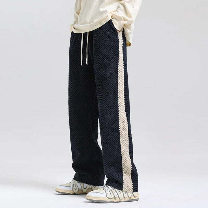 Black textured wide-leg pants with cream side stripes and drawstring waist, styled with white sneakers