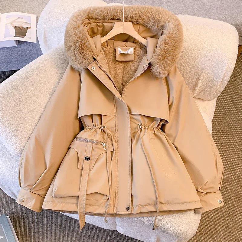 Beige winter parka jacket with fur-lined hood and adjustable waist, laid on a white textured armchair