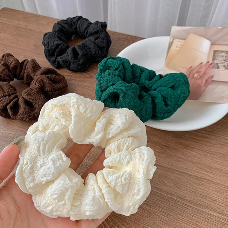 Soft textured fabric scrunchies in cream, green, black, and brown colors on wooden table and white plate