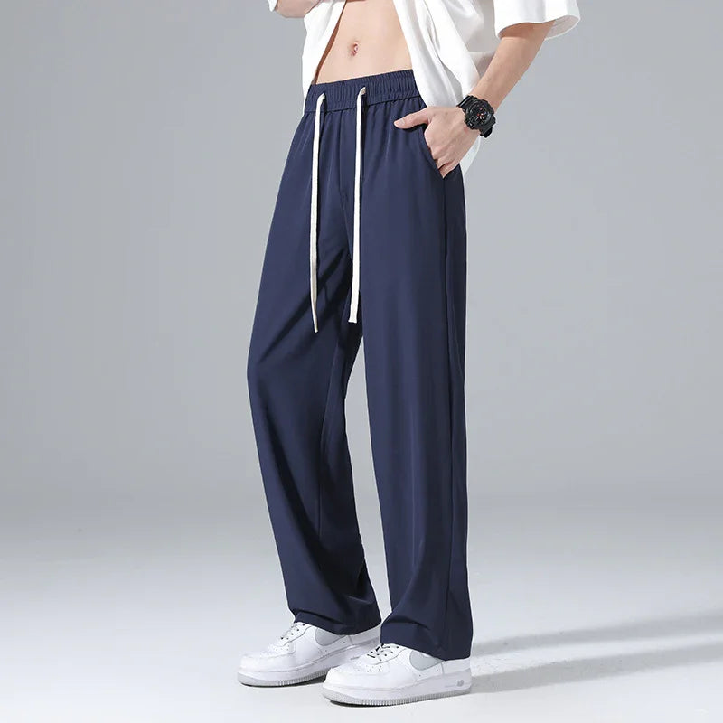 Man wearing navy blue wide-leg drawstring pants with white sneakers and a white shirt against gray background