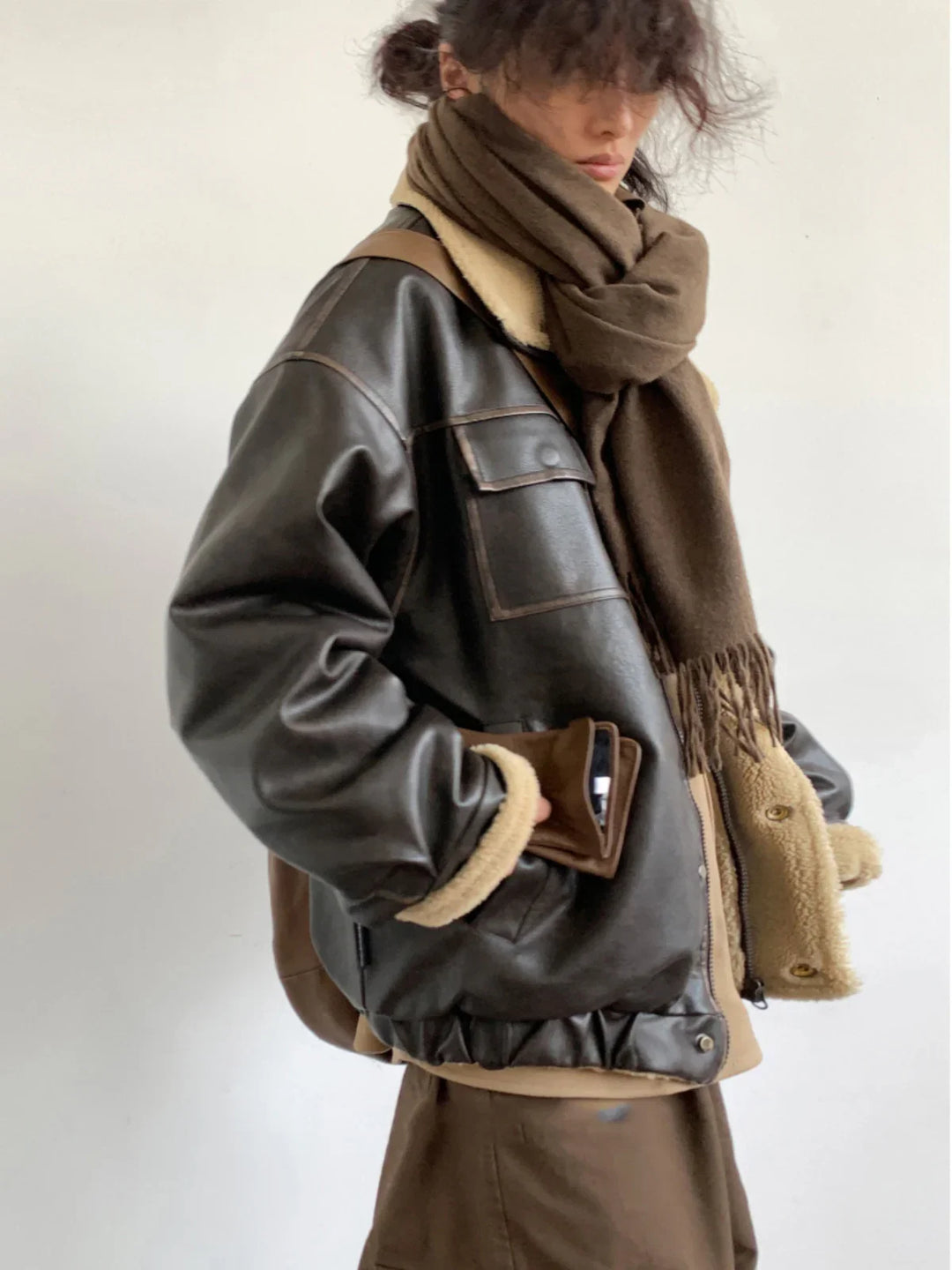 Person wearing dark brown leather bomber jacket with shearling lining and a thick brown scarf