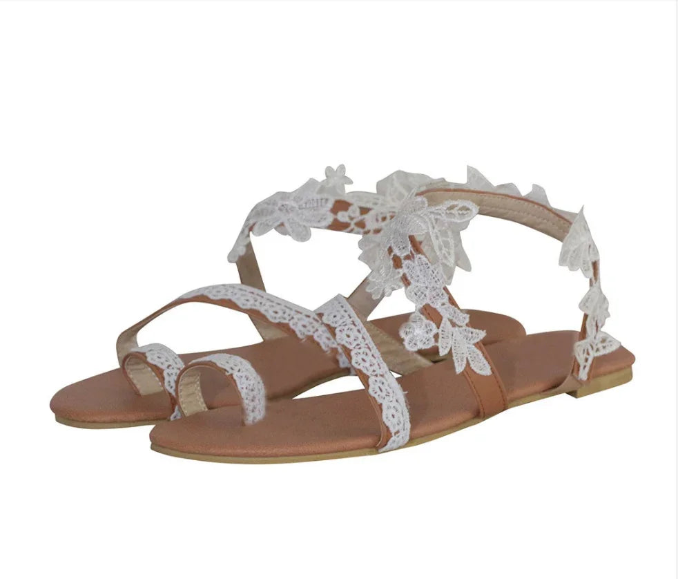 Brown flat sandals with white floral lace ankle and toe straps on a white background