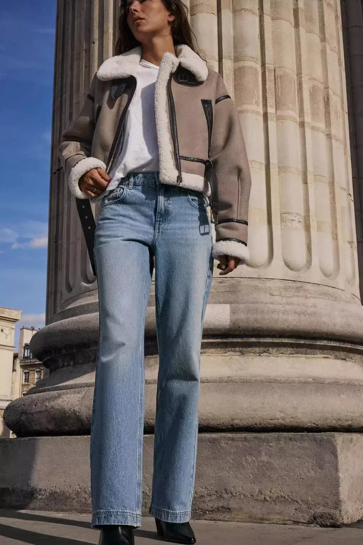 Woman in shearling jacket, white tee, and light blue jeans standing by a large stone column outdoors