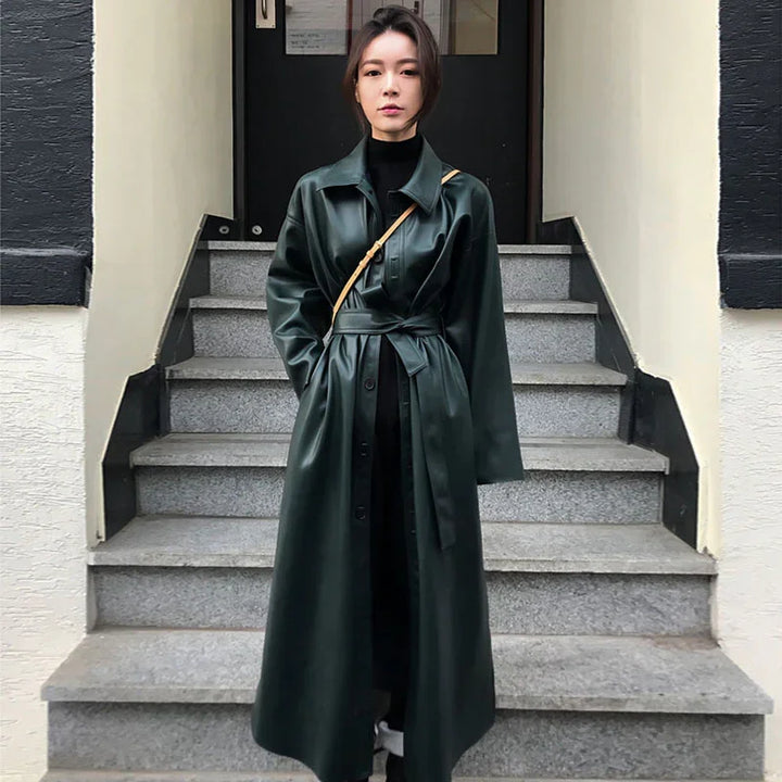 Woman wearing long dark green leather trench coat standing on gray stone steps outdoors