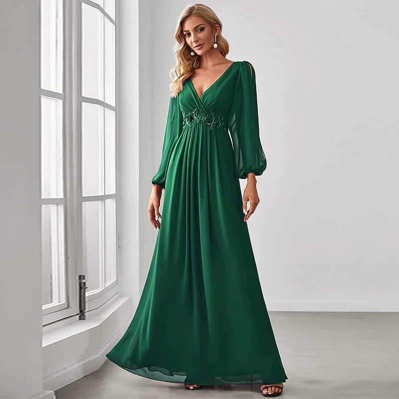 Blonde woman in elegant emerald green long dress with puffed sleeves standing by large window