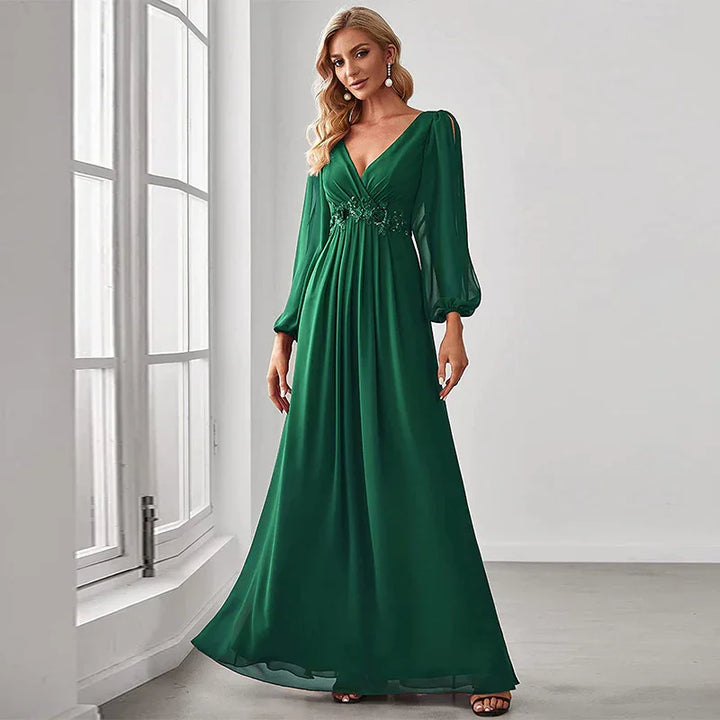 Blonde woman in elegant emerald green long dress with puffed sleeves standing by large window