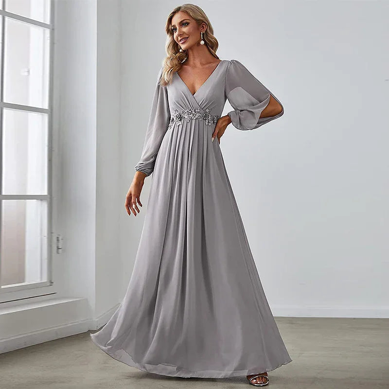 Woman wearing elegant gray long sleeve V-neck evening gown with floral waist embellishment in bright room