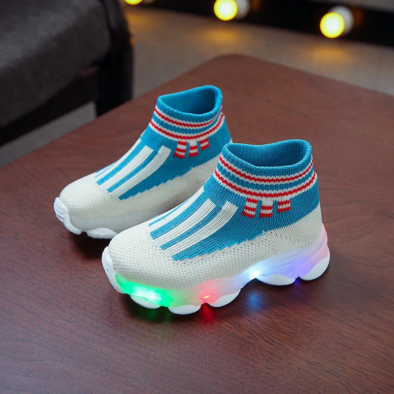 Children's blue and white LED light-up sock sneakers with red striped ankle cuffs on wooden table