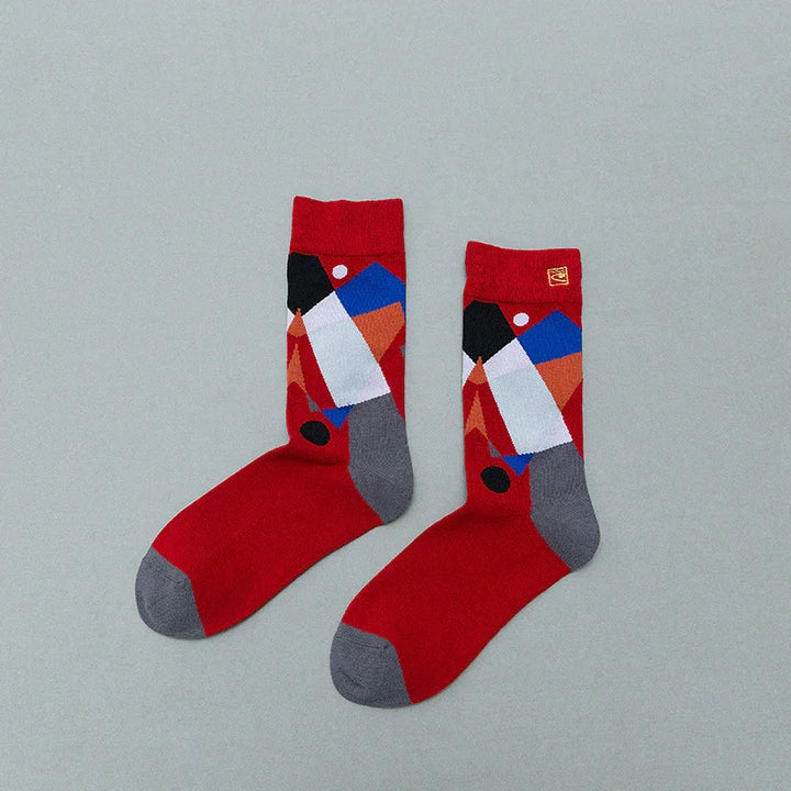 Pair of red socks with gray toes and heels, featuring abstract geometric pattern in blue, white, black, and orange