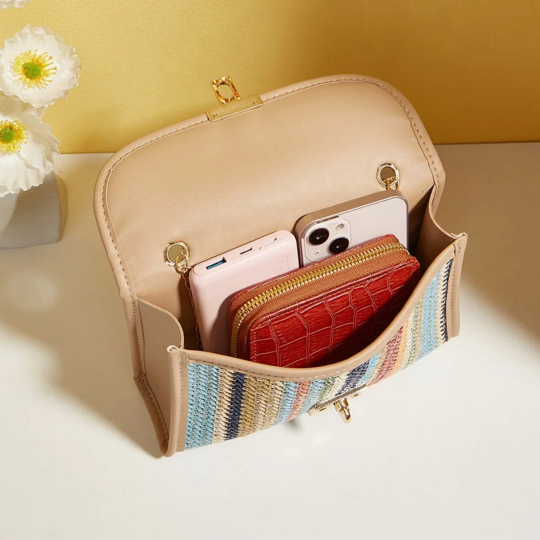 Beige handbag with multicolor woven front pocket holding a red wallet and two smartphones on white surface