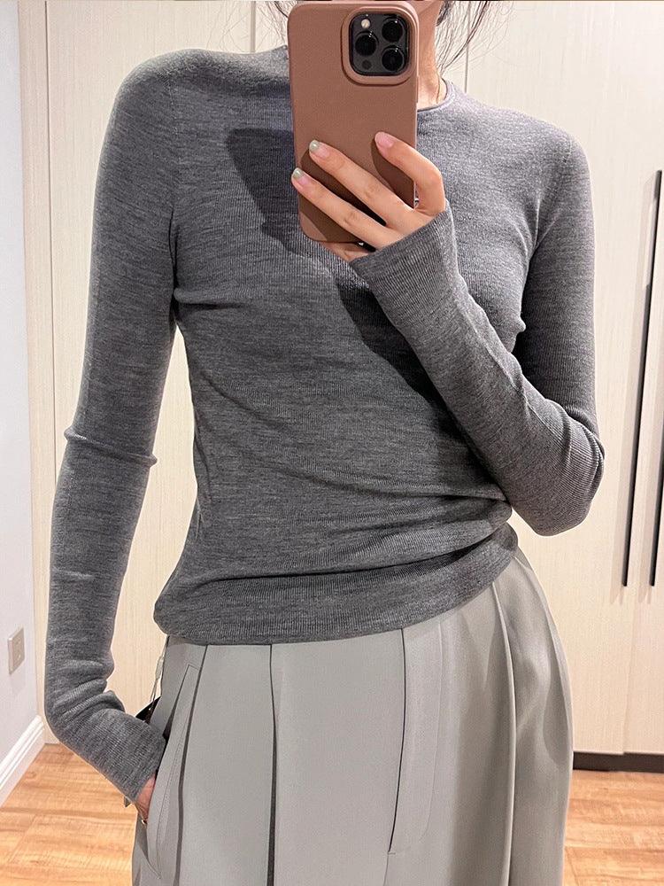Person wearing a fitted grey long-sleeve top paired with light grey pleated trousers taking a mirror selfie