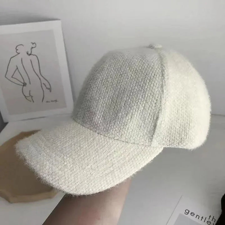 Soft textured beige baseball cap held in hand with minimalist line art and wooden tray in background