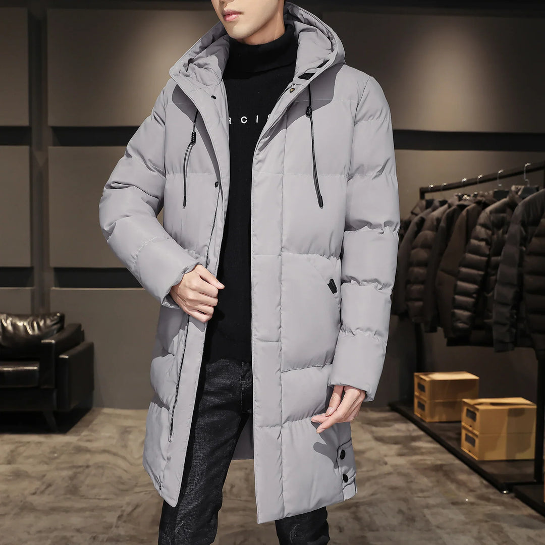 Man wearing long gray padded winter coat with hood in modern store interior