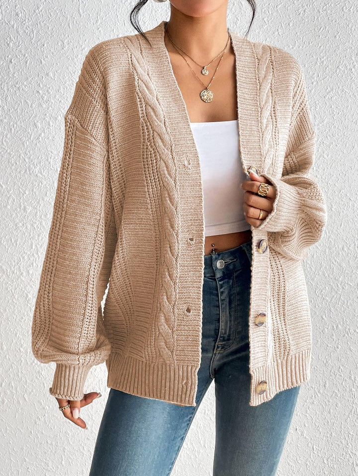 Woman wearing beige knit cardigan with cable knit detail over white crop top and blue jeans