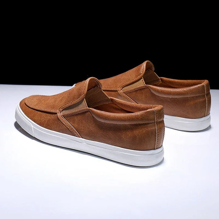 Brown slip-on casual shoes with white rubber soles on a white surface and black background
