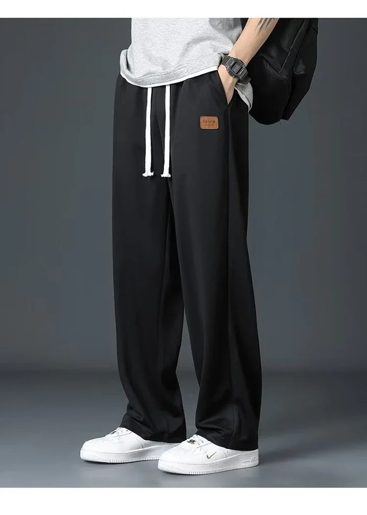 Man wearing black wide-leg pants with white drawstrings and white sneakers against gray background