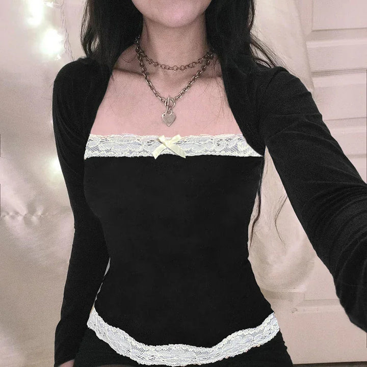 Woman wearing black long-sleeve velvet top with white lace trim and bow detail, layered silver chain necklaces