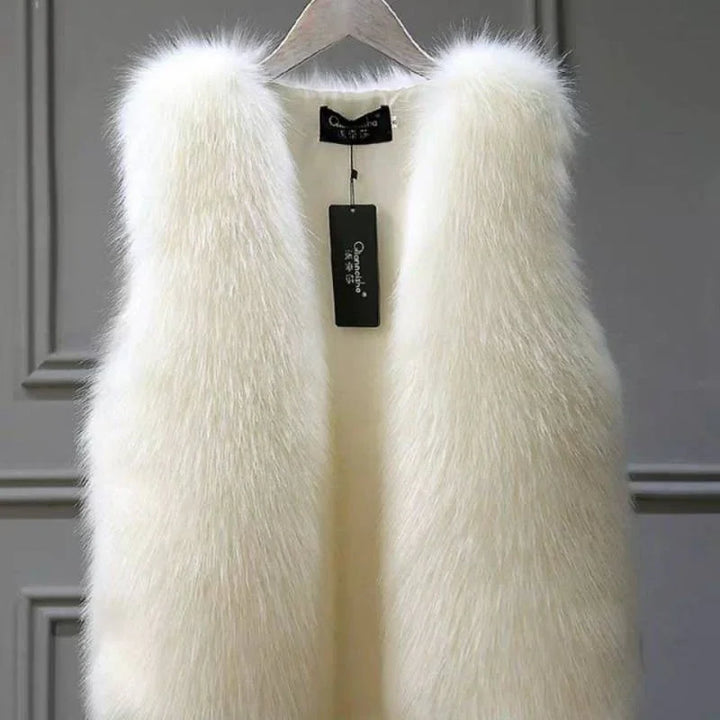 White faux fur vest hanging on wooden hanger with black brand tag against gray paneled wall