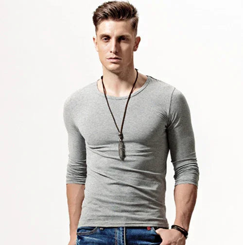 young man wearing fitted gray long-sleeve shirt and blue jeans with pendant necklace