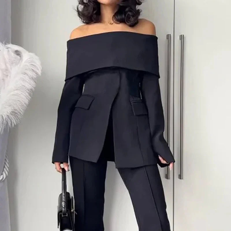 Woman wearing a black off-shoulder blazer and matching pants holding a black handbag indoors