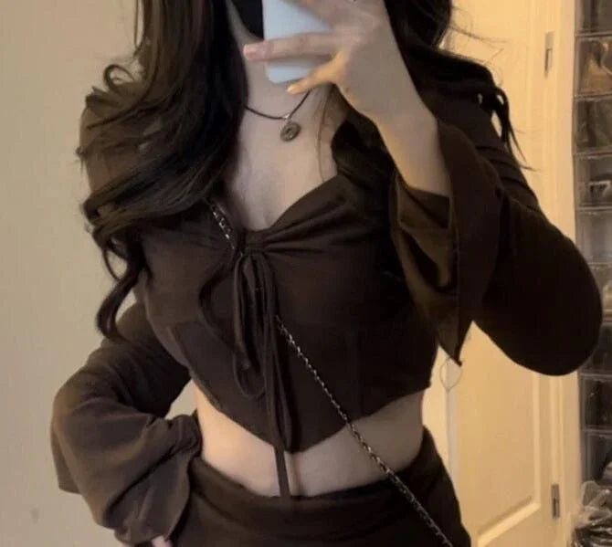 Woman wearing brown long-sleeve cropped top with tie detail and matching skirt taking mirror selfie